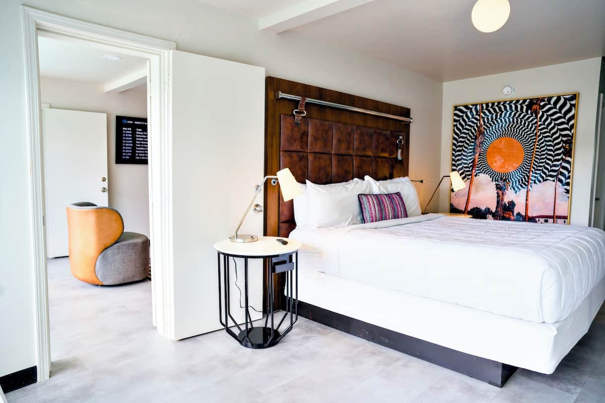 A modern bedroom with a large bed, a wooden headboard, a side table, and a unique wall painting.