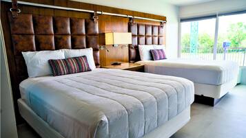 Hotelkamer met twee bedden, een houten hoofdbord, een nachtkastje en een raam met uitzicht op groen.