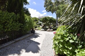 A pathway lined with gravel and greenery, leading to a building with a white facade and a visible antenna.
