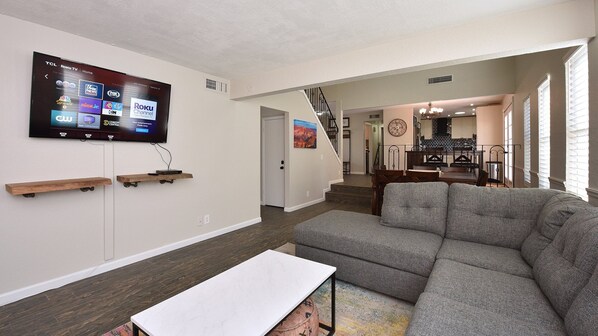 A living room with a gray sofa, a white coffee table, and a mounted TV displaying Roku TV interface. - Desert Escape l 2 Masters l Heated Pool (Mesa)