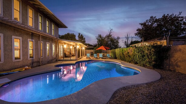 A swimming pool with a curved edge, surrounded by a patio area with chairs and an umbrella. - Desert Escape l 2 Masters l Heated Pool (Mesa)