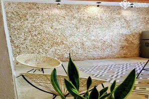 Una habitación con pared texturizada, una silla de fibras naturales y un suelo con diseño.