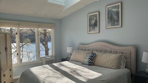 A bedroom with a bed, two wall-mounted lamps, a window with a view of trees and a lake, and a skylight. - Waterfront, private dock, neighborhood beach (Saunderstown)