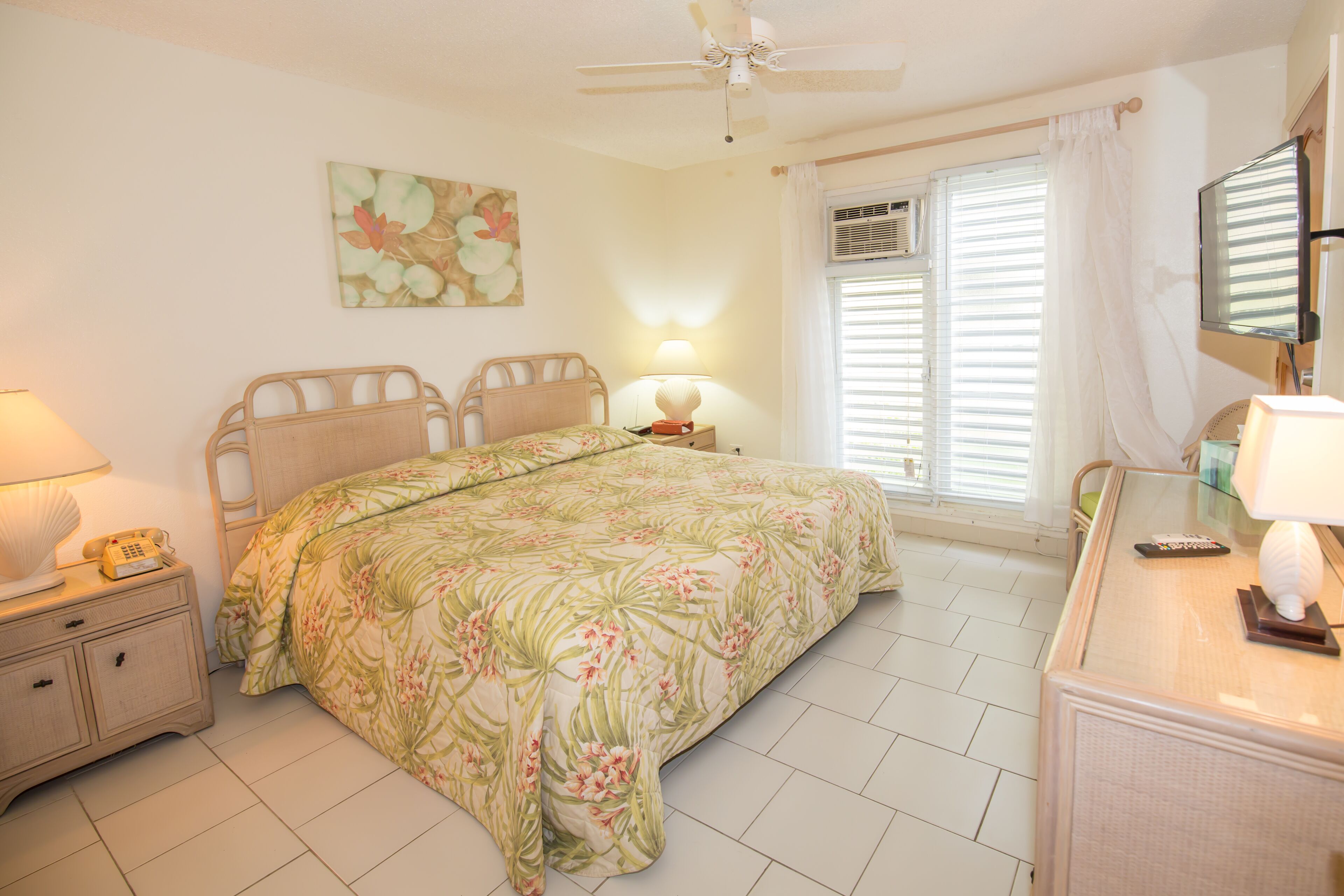 Quarto com cama, mesa de cabeceira, abajur e ventilador de teto.
