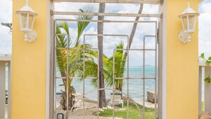 A yellow gate with a metal grid, leading to a beach with palm trees and a view of the ocean. - "ISLAND DREAMS" Spectacular Views, Pool, Beach, AC, Internet, 2 BR 2 Bath (Christiansted,)