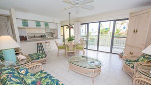 A spacious living area with wicker furniture, a glass coffee table, and a kitchen in the background. - "ISLAND DREAMS" Spectacular Views, Pool, Beach, AC, Internet, 2 BR 2 Bath (Christiansted,)