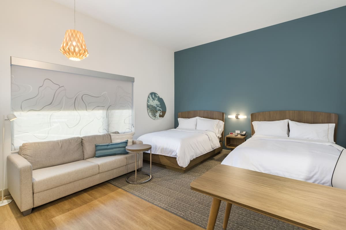 Ein modernes Hotelzimmer mit einer Couch, zwei Einzelbetten, einem kleinen runden Tisch und einer hölzernen Bank.