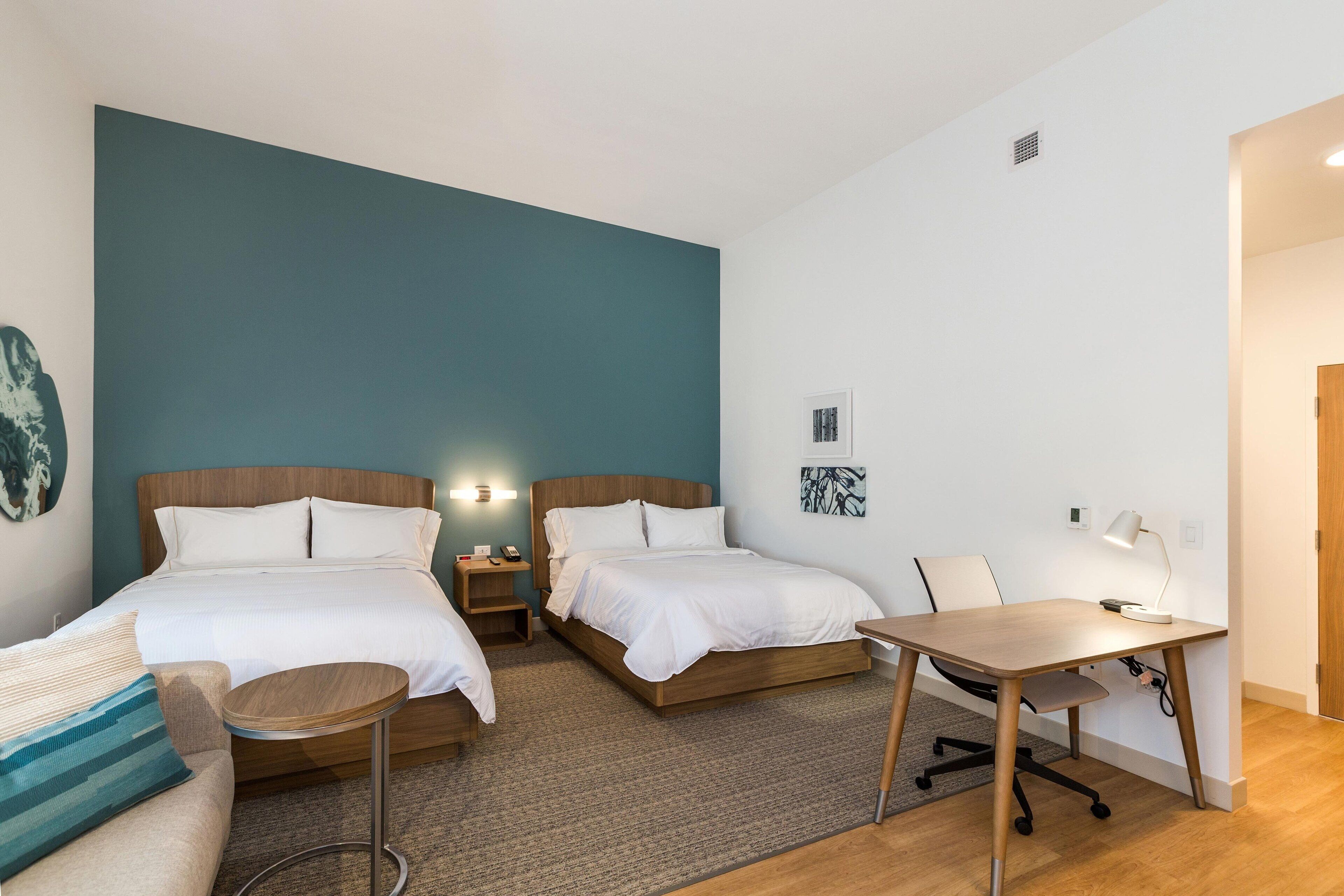 Habitación de hotel con dos camas, un escritorio, una silla y una mesita redonda.