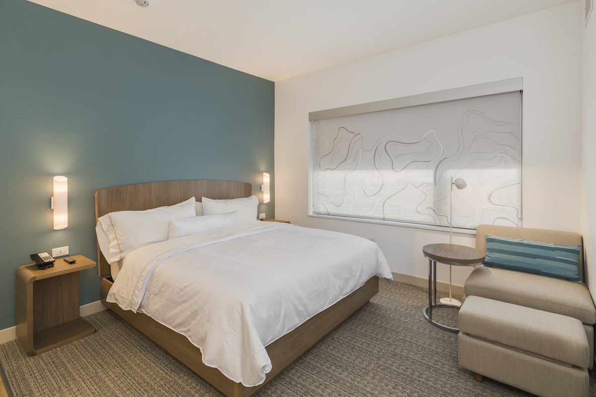 Ein modernes Hotelzimmer mit einem großen Bett, Nachttischen, einem runden Beistelltisch, einer Couch und einer dekorativen Wandverkleidung.