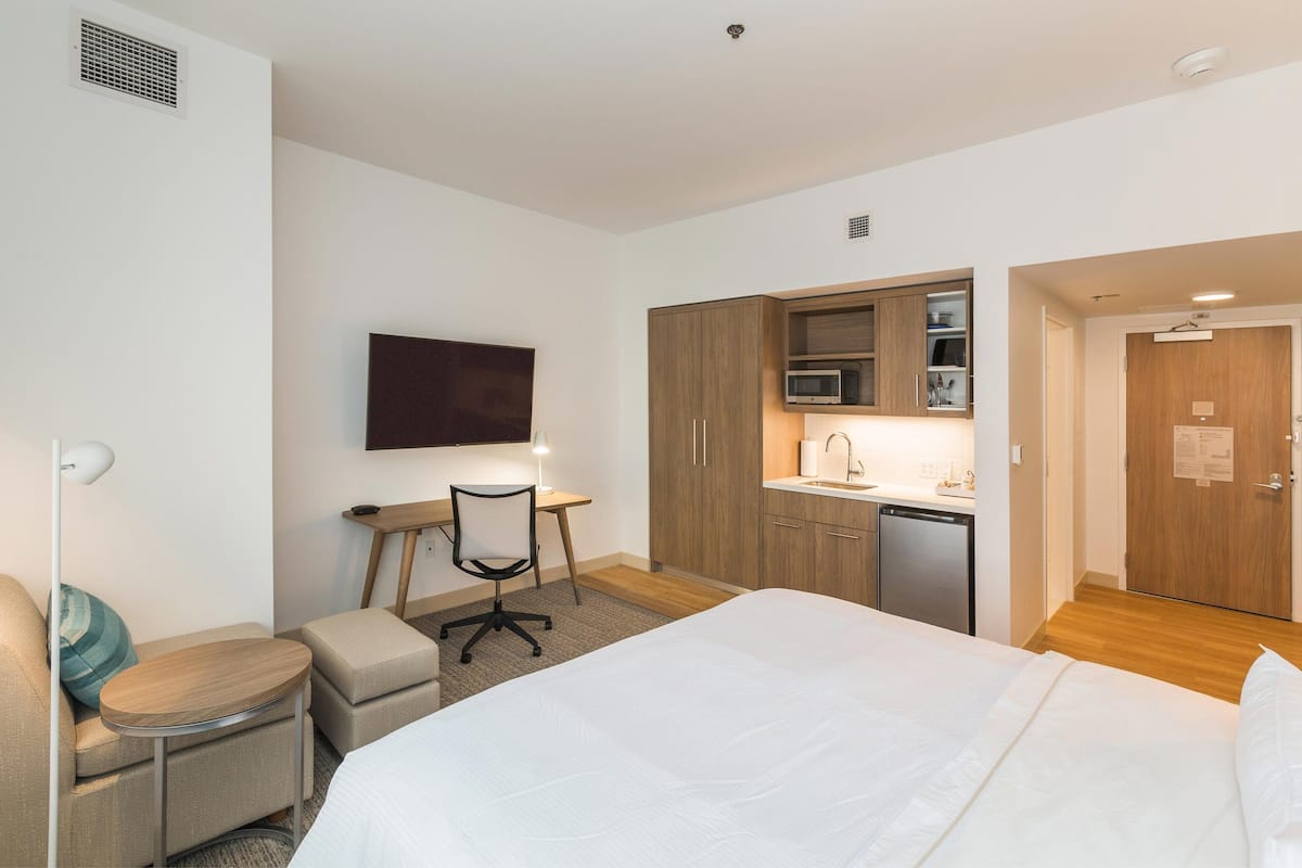 Ein Hotelzimmer mit Bett, Schreibtisch, Stuhl, Fernseher, Mikrowelle und einer kleinen Küchenzeile.
