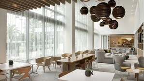 Un moderno vestíbulo de hotel con diversas zonas de estar, incluyendo mesas y sillas, y un área central con sofás.