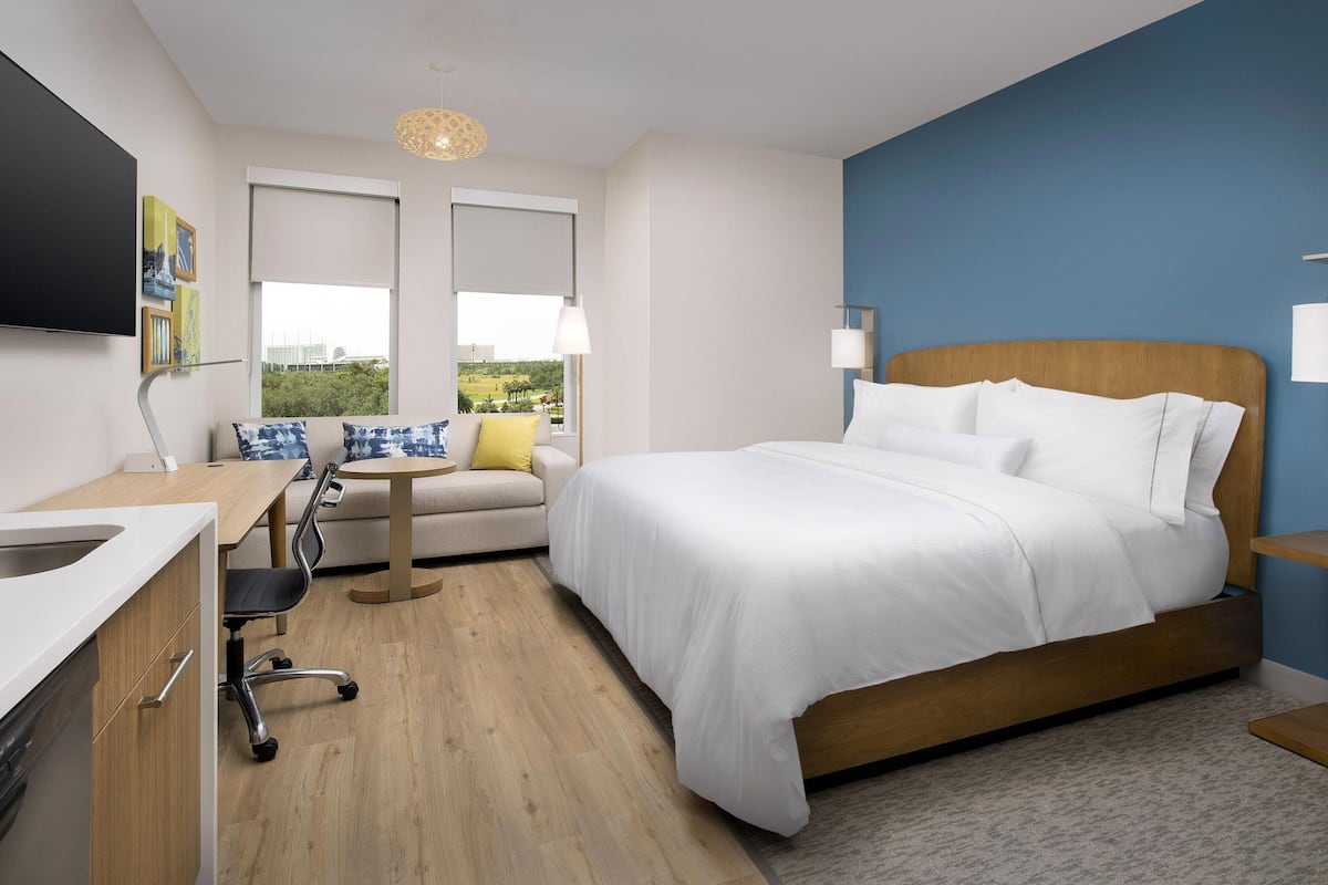 A modern hotel room with a bed, a desk, a chair, and a view of the outdoors.