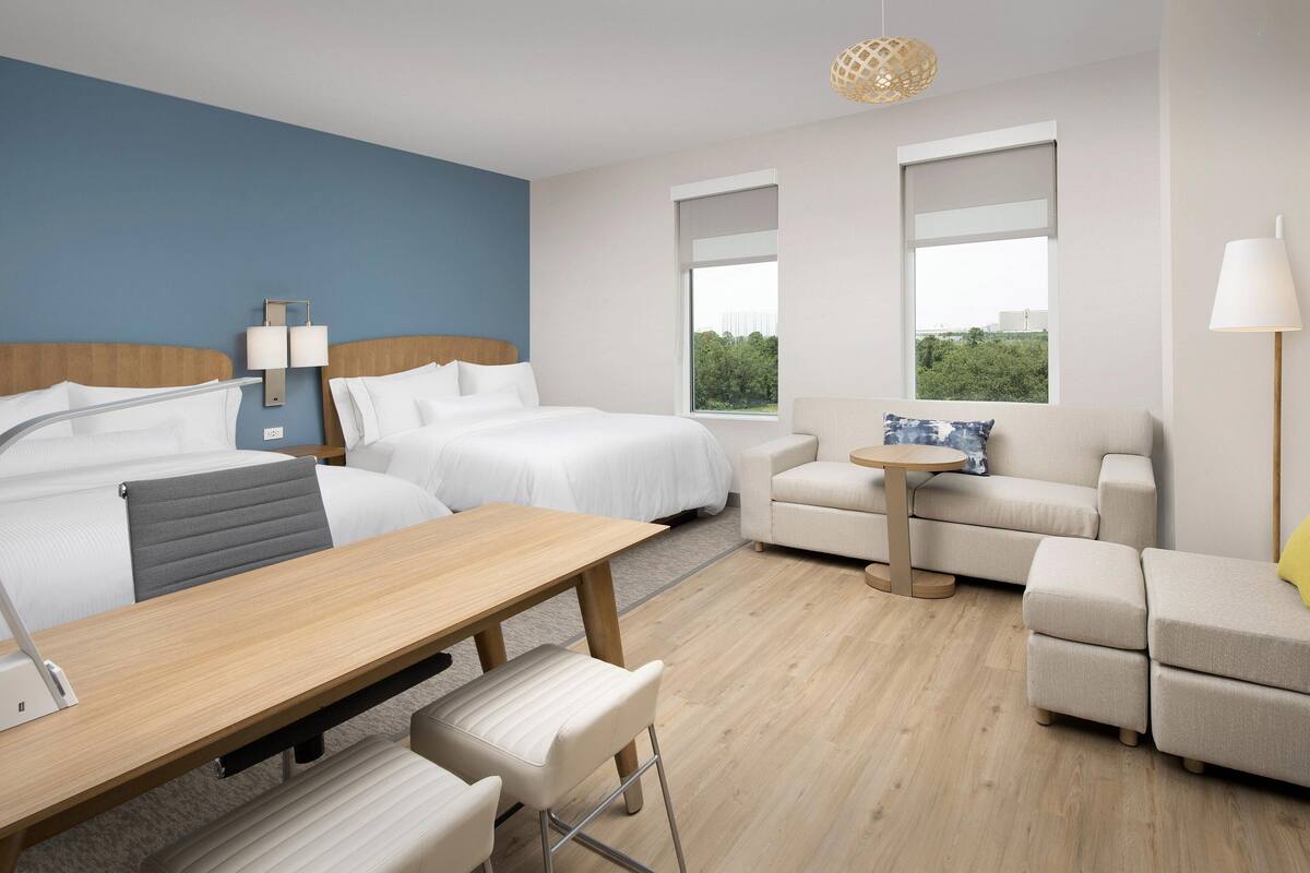 A hotel room with two beds, a desk, a chair, a sofa, and a small table.
