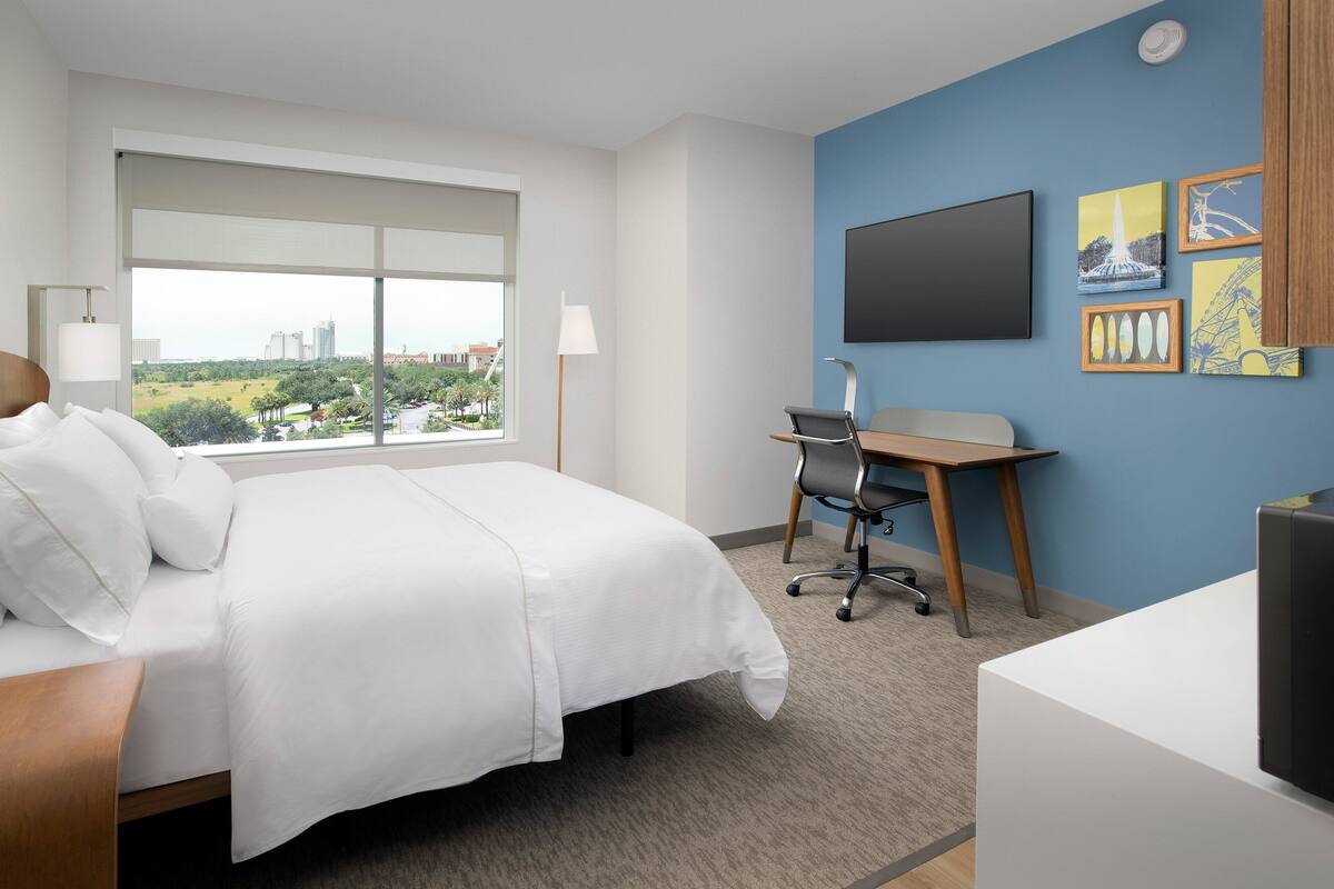 A hotel room with a bed, desk, and large window.