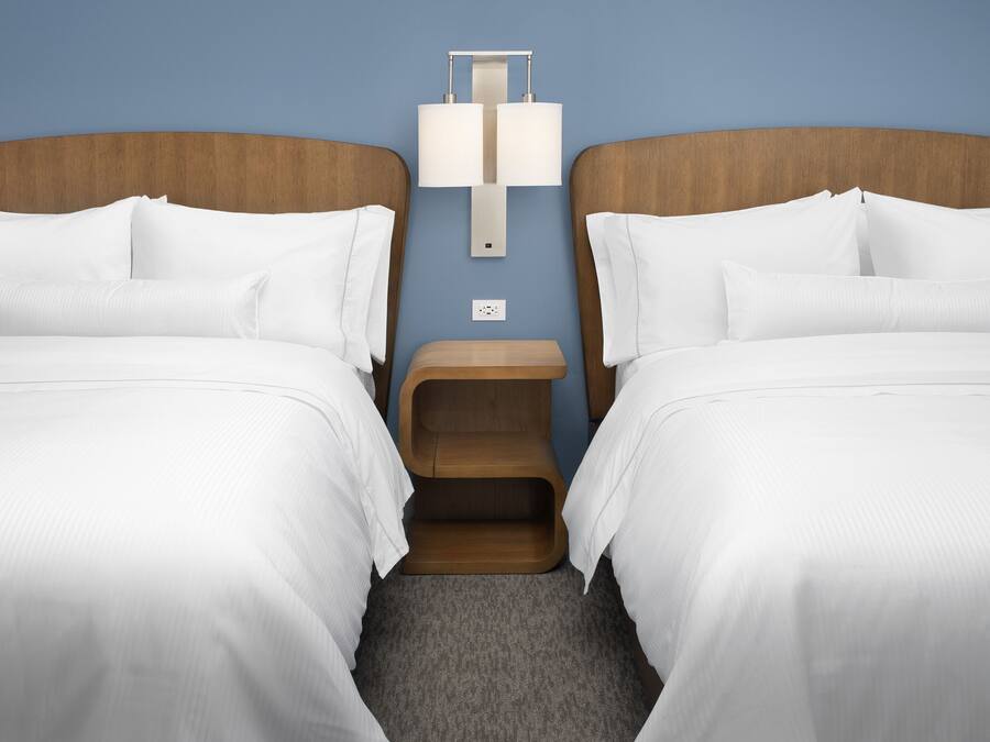 A hotel room with two beds, a nightstand, and a wall-mounted lamp.
