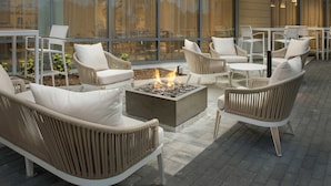 Un espacio al aire libre con mobiliario de mimbre y una chimenea central.