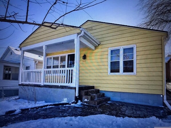 A single-story house with a porch, a small front yard, and a snow-covered ground.