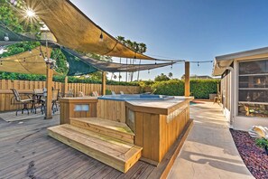 En træterrasse med jacuzzi, udendørs møbler og et overdækket område med lyskæder.
