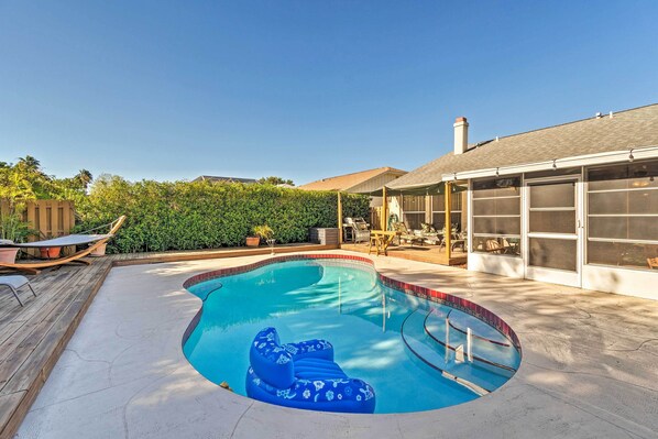 En have med swimmingpool, træterrasse og havemøbler.