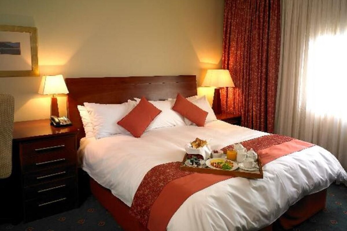 Une chambre d’hôtel avec un grand lit, deux tables de chevet avec des lampes, un plateau de petit-déjeuner et une fenêtre avec des rideaux.
