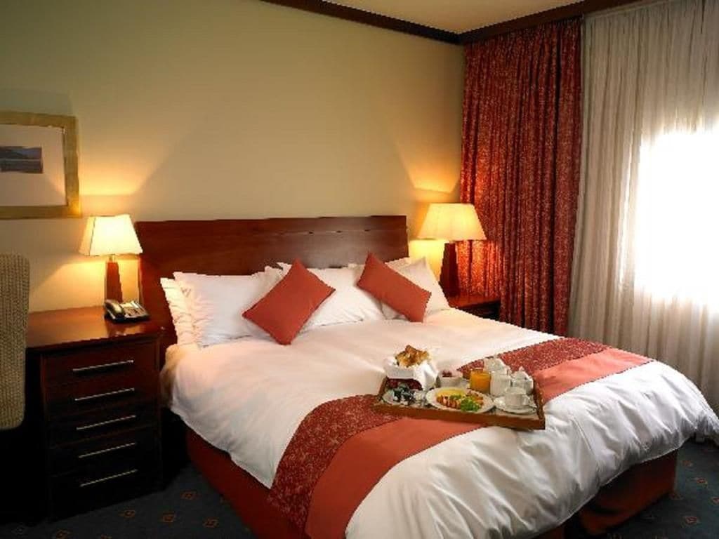 A hotel room with a large bed, two bedside tables with lamps, a tray of breakfast items, and a window with curtains.