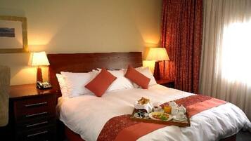 A hotel room with a large bed, two bedside tables with lamps, a tray of breakfast items, and a window with curtains.