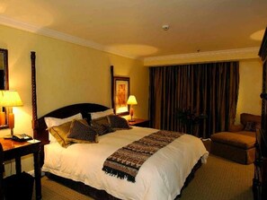 Une chambre d’hôtel avec un grand lit, deux tables de chevet avec des lampes, une chaise et un rideau.