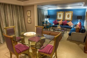 Une pièce comprenant une table à manger avec un plateau en verre, entourée de chaises, d’un ensemble de canapés et d’un fauteuil à motifs.