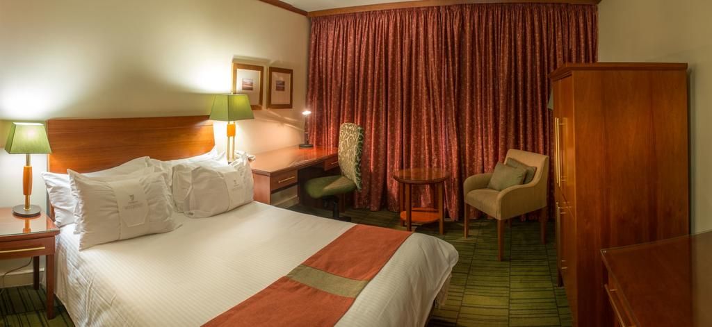 Una habitación de hotel con cama, dos sillas, escritorio y armario.