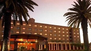 A large hotel with multiple floors, a central entrance with a canopy, and palm trees in the foreground. - Peermont Walmont Ambassador at the Grand Palm (Gaborone)
