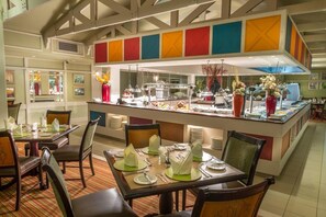 A hotel dining area with tables set for guests, a buffet counter with various food items, and a modern ceiling design. - Peermont Walmont Ambassador at the Grand Palm (Gaborone)