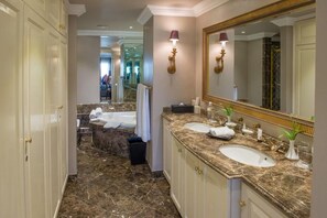 Une salle de bain luxueuse avec un sol en marbre, deux vasques, un grand miroir et un meuble-lavabo doté d’un plan de toilette en marbre.