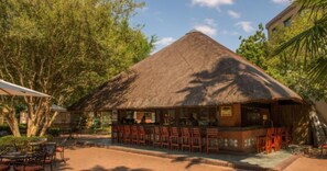 Een buitengewoon terras met rieten dak, diverse zithoeken en uitzicht op groene omgeving.