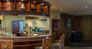 A bar area with a curved counter, bar stools, and a television screen. - Peermont Walmont Ambassador at the Grand Palm (Gaborone)