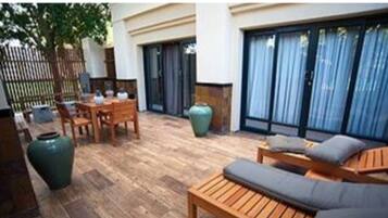 An outdoor patio with wooden furniture, a large green vase, and a wooden table.
