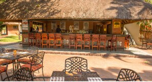 Un restaurant doté d’un toit de chaume, d’une terrasse avec des chaises en métal et d’un espace bar.