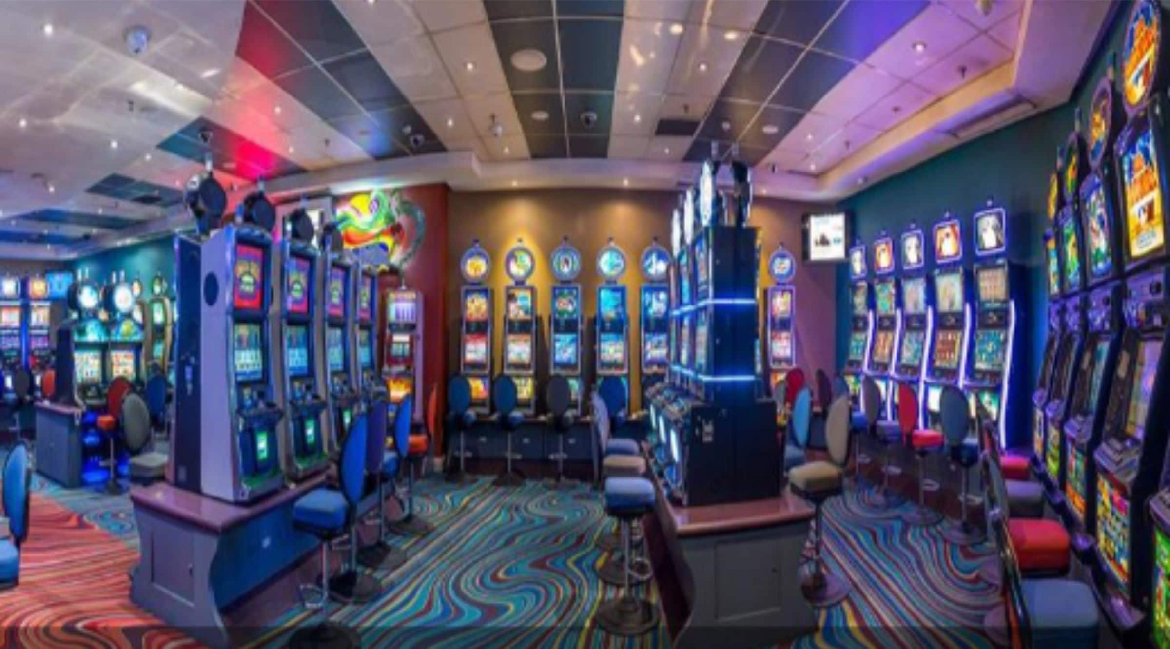 A casino with multiple slot machines, a colorful carpet, and a ceiling with recessed lighting.