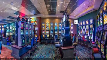A casino with multiple slot machines, a colorful carpet, and a ceiling with recessed lighting.