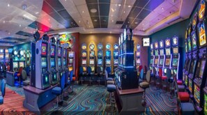 Ein Casino mit mehreren Spielautomaten, einem farbenfrohen Teppich und einer Decke mit eingelassener Beleuchtung.
