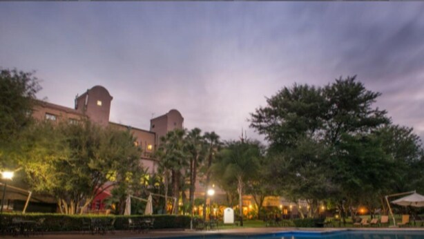 A hotel with a pool, surrounded by trees and a large building with a dome structure in the background. - Peermont Walmont Ambassador at the Grand Palm (Gaborone)