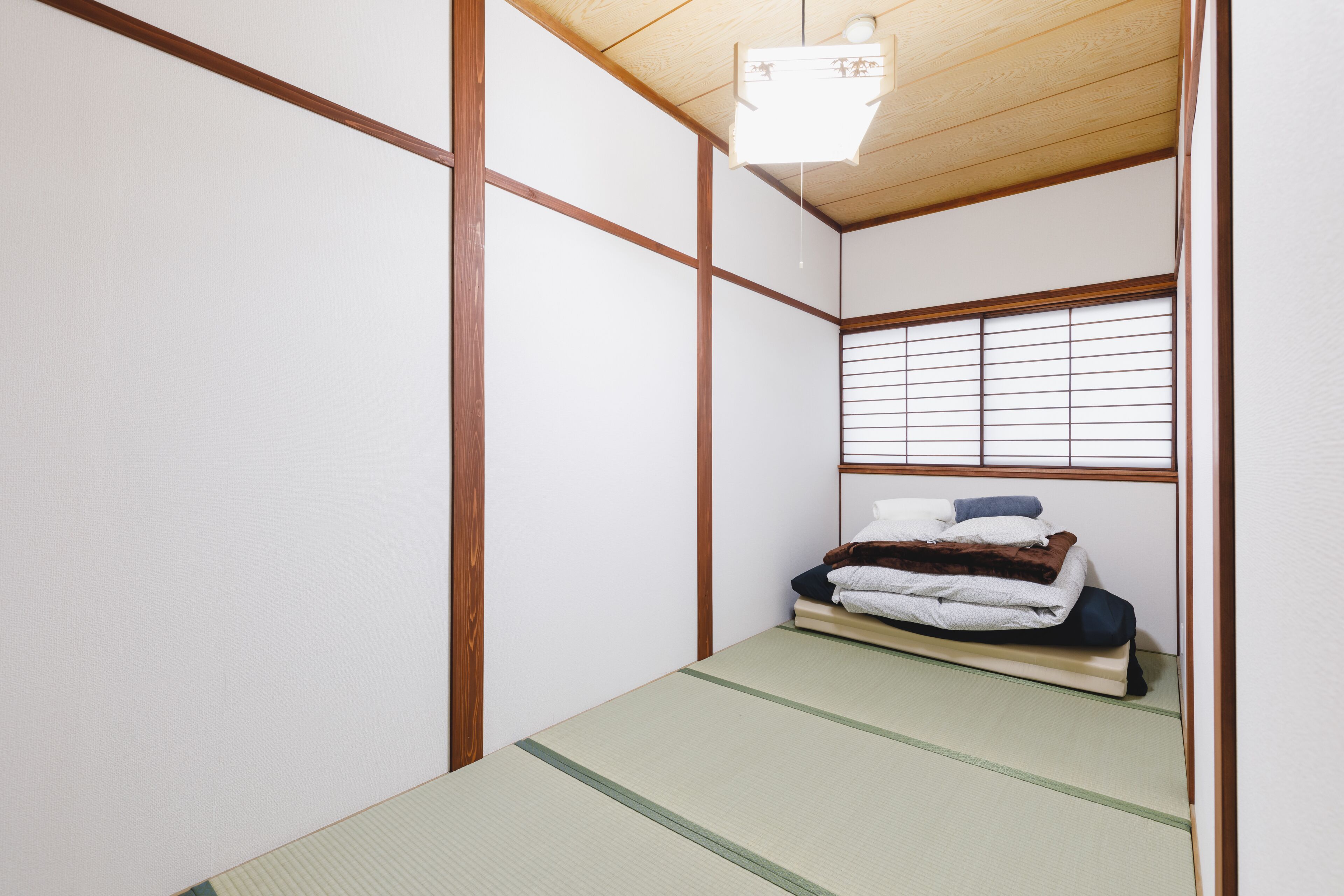 A traditional Japanese room with tatami flooring, a low bed with a futon, and shoji screens.
