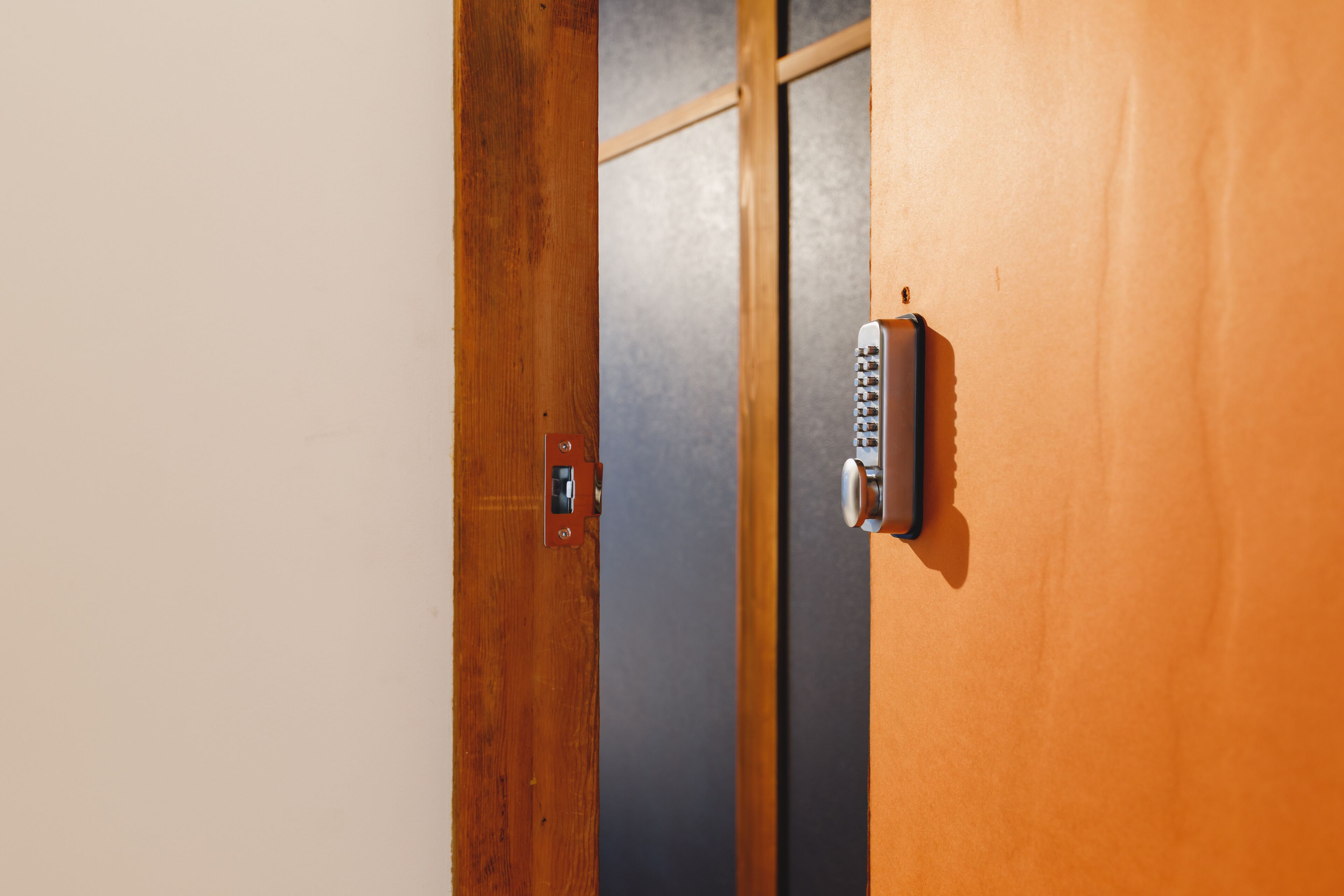 A wooden door with a keypad lock and a small electronic device on the door frame.