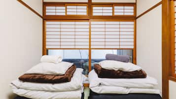 A traditional Japanese room with tatami flooring, a shoji screen, and two beds with pillows and blankets.