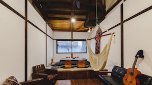A cozy living room with a hammock, leather sofas, a wooden coffee table, and a guitar. - Couch Potato Hostel (Matsumoto)