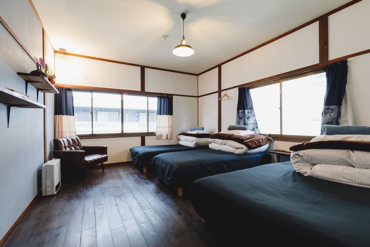 Ein Hotelzimmer mit zwei Einzelbetten, einer Schlafcouch, einem kleinen Tisch und einem Fenster mit Vorhängen.