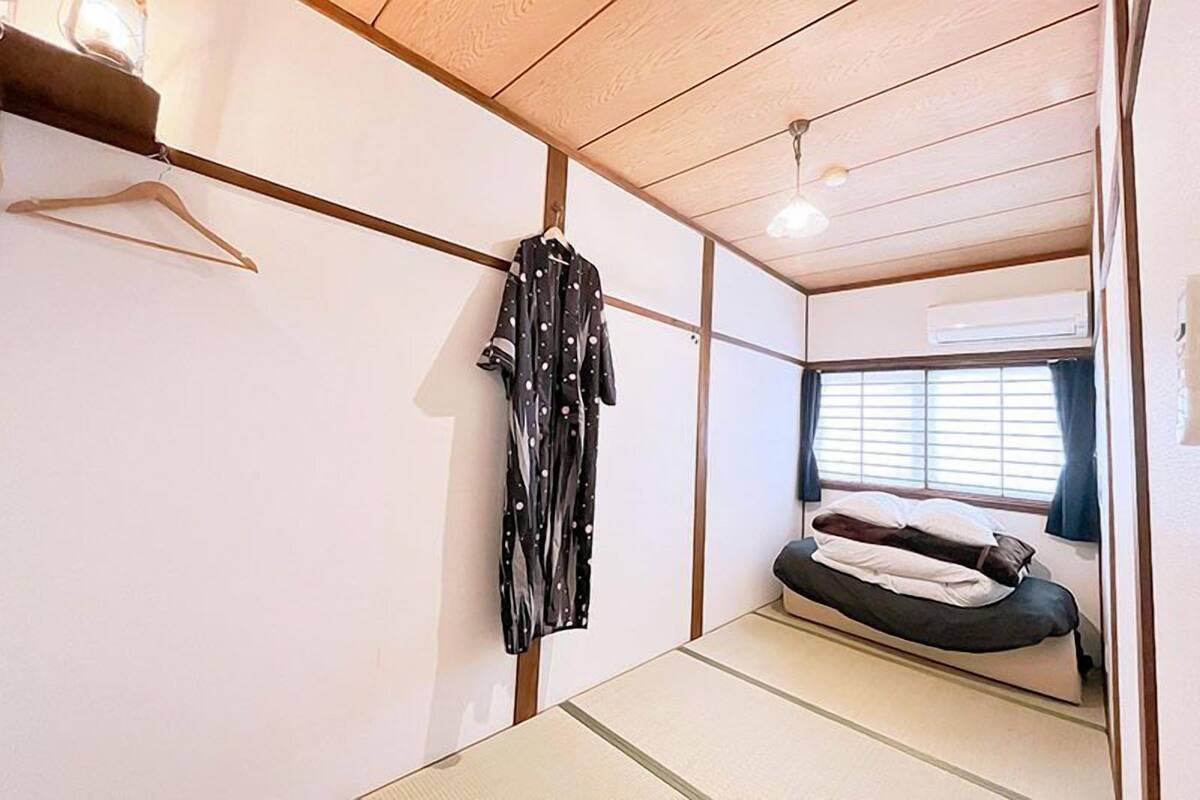 Ein kleines Zimmer mit Bett, Kleiderhaken und einem fenster mit Vorhängen.