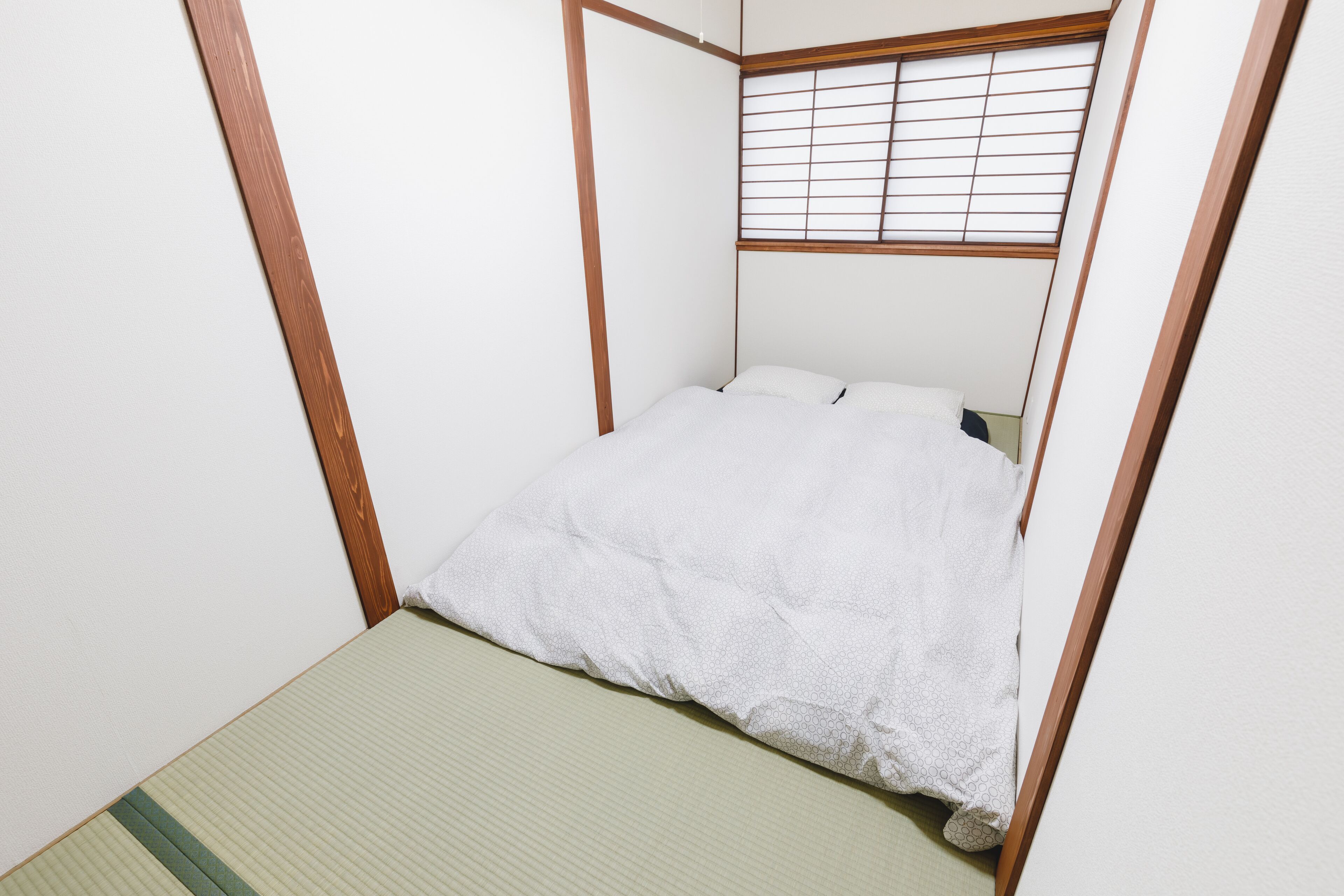 Une petite chambre avec un lit simple, un cadre en bois et une fenêtre équipée de stores horizontaux.