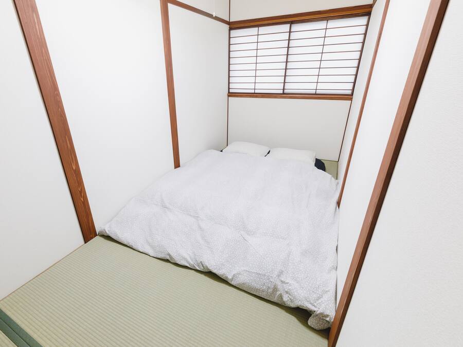 Une petite chambre avec un lit simple, un cadre en bois et une fenêtre équipée de stores horizontaux.