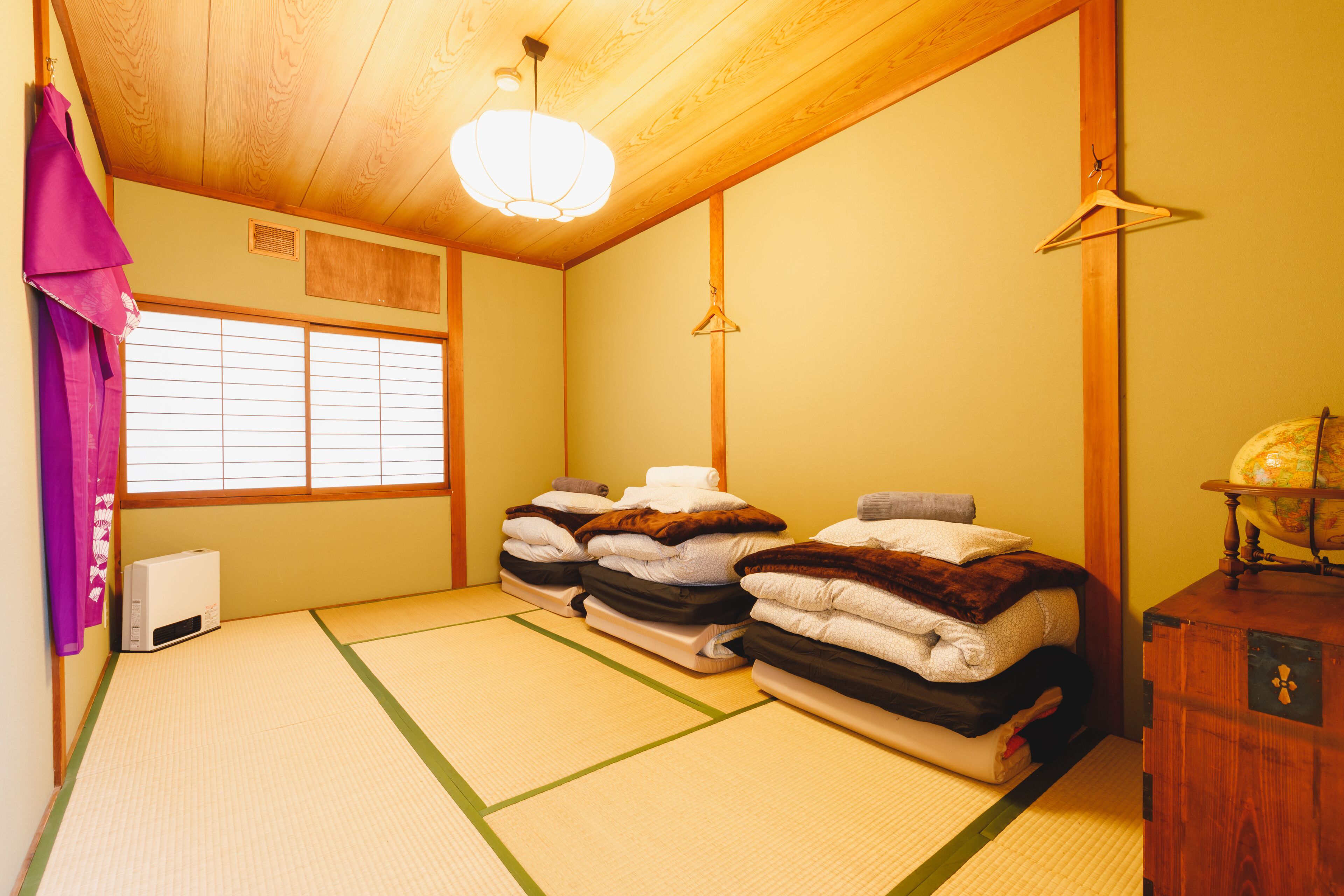 Une pièce de style japonais traditionnel, avec un sol recouvert de tatamis, un plafond en bois et un lit où les couvertures sont soigneusement pliées.