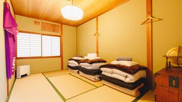 Une pièce de style japonais traditionnel, avec un sol recouvert de tatamis, un plafond en bois et un lit où les couvertures sont soigneusement pliées.